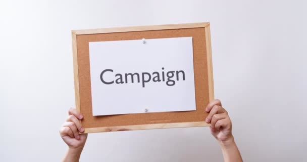 女性の手は コピースペースと白いスタジオの背景にキャンペーンという言葉でボード上の紙を示しています — ストック動画