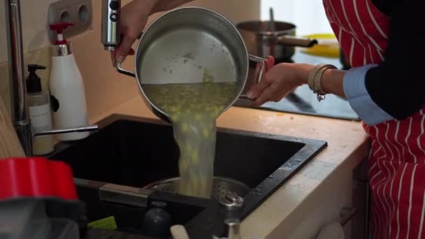 コリアンダーを使用したキッチンシンクで茹でたジャガイモ生地のランプの女性の排水 ミディアムショット — ストック動画