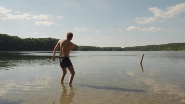 晴れた日にポーランドのグリーボキー湖で石をスキップする白人男性 幅が広く動きが遅い — ストック動画