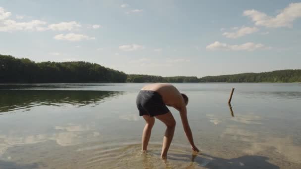 ポーランドのイェジオーロ グレボキーの静かな湖に石を投げる白人男性 ワイドショット — ストック動画