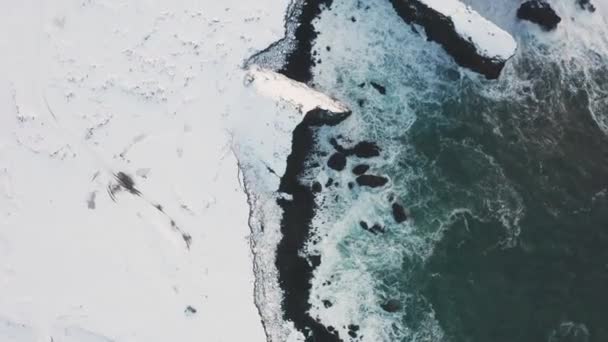 雪が黒い砂の一部を覆っている間 アイスランドの黒いビーチの美しいドローンは 海と曇りの天気の高い波を示しています — ストック動画