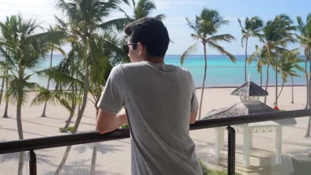年轻的成年男子从房间阳台俯瞰加勒比海滩 美丽的海洋风景 旅游主题 — 图库视频影像