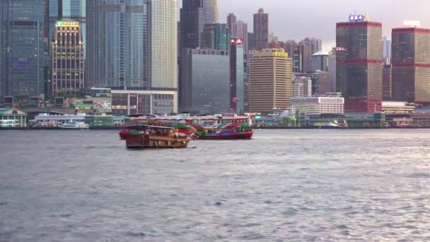 香港水域船只在多云天气下沿维多利亚港航行的固定宽角镜头 船尾为建筑物及摩天大楼 — 图库视频影像