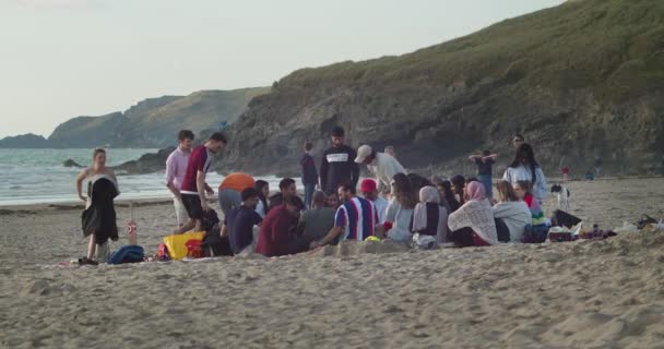 砂の海岸に座っている若者の多文化グループパーランポールビーチで夏を楽しむ コーンウォール イギリス イギリス — ストック動画