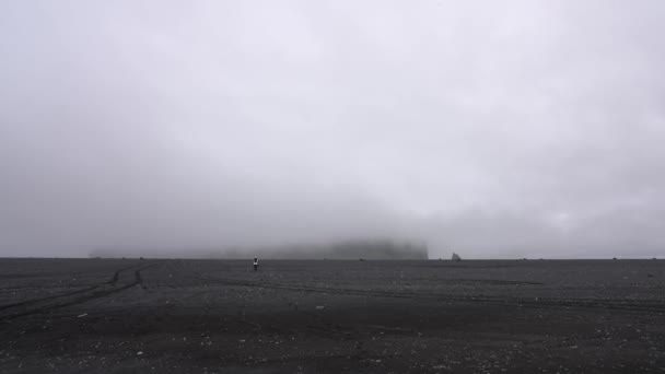 アイスランドの神秘的な曇りの日の間に火山砂の砂漠を歩く人を示す広いショット島 — ストック動画
