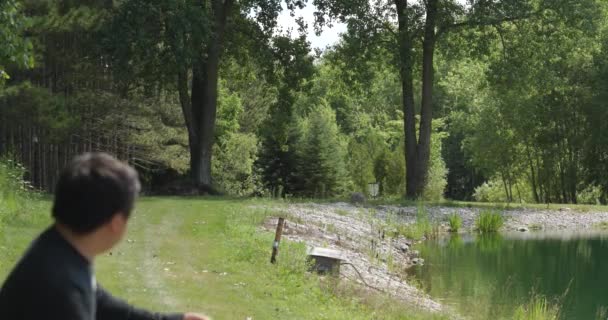 池の横にディスクゴルフを投げる男の側面図 — ストック動画