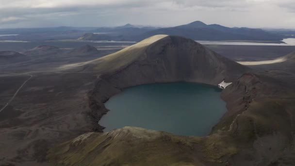 灰色の暗い日の間にアイスランド島の黒い砂の砂漠に囲まれた美しいクレーター湖の上のドローン飛行 — ストック動画