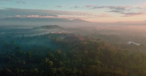 インドネシアのボロブドゥール寺院とオレンジの日の出に周囲の山々を見渡す美しいドローン飛行 — ストック動画
