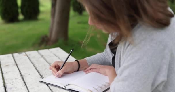 緑豊かな庭に座って日記を書いている若い白人女性は — ストック動画