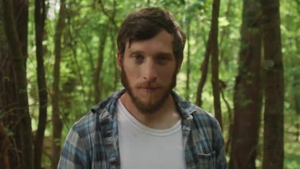 Выразительный Бородатый Молодой Человек Смотрит Прямо Камеру Лесным Фоном — стоковое видео
