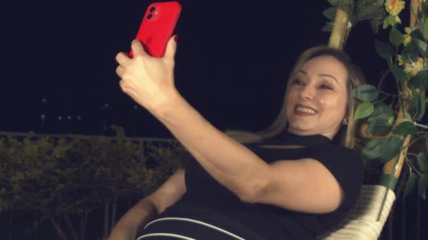 Smiling Hispanic Woman Taking Selfie While Leaning Back Swing Chair — Stock Video