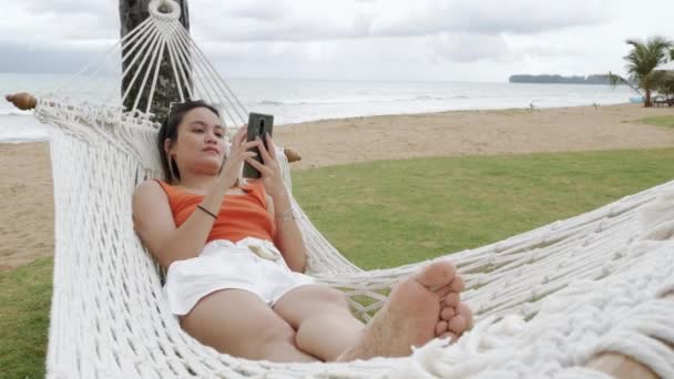 亚洲女人度假时在海滨椰子树下的吊床上休息 — 图库视频影像