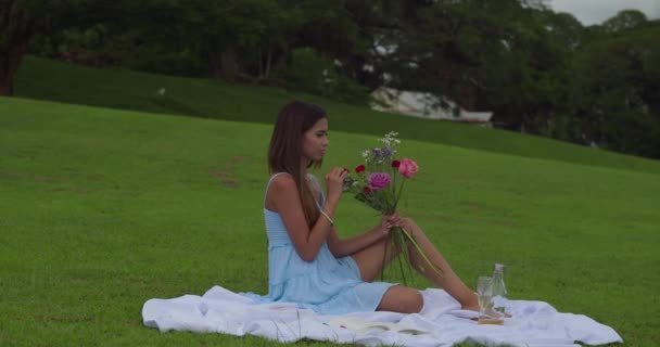 ピクニックのセッティングで花の花束を持っている若い女性 — ストック動画