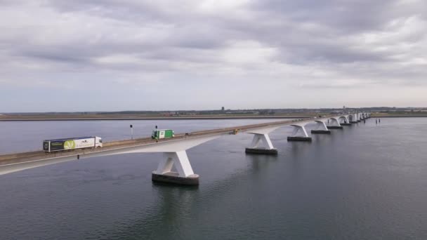 オランダ南西部の7キロメートルのゼーラント橋を横断する複数のトラックやその他の車両が 曇りの朝に走行します 空中スライダーショット — ストック動画