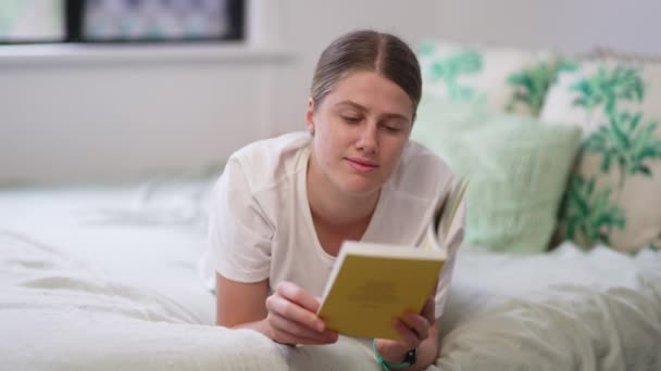 Νεαρή Λευκή Γυναίκα Ξαπλωμένη Στο Κρεβάτι Διαβάζοντας Βιβλίο Και Γυρίζοντας — Αρχείο Βίντεο