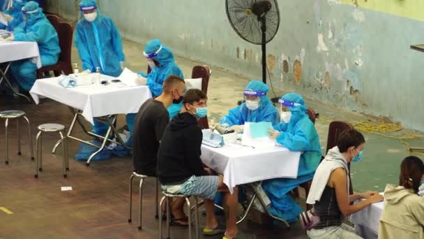 昼間にベトナムのCovid 19のための一時的なワクチンセンターでコロナウイルスのための2番目のワクチン用量を取得するために来る地元住民の上に撮影された高角度 — ストック動画
