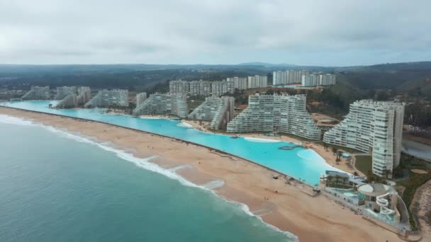 チリのアルガルロノで砂のビーチを打つ海に近い世界最大のスイミングプールとリゾートの空中軌道 — ストック動画