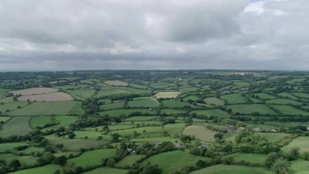 イギリスのデヴォンのダンプドンにある森と劇的な雲に囲まれた農場の土地のエーカーを表示する上空を飛ぶ — ストック動画