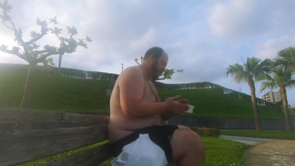 衣衫褴褛的男人吃完垃圾食品后 用餐巾擦拭手和嘴 — 图库视频影像