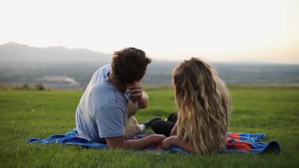 毛布の上に寝そべって芝生の上でピクニックをしているかわいいボーイフレンドとガールフレンドのスローモーションショット 彼氏が横になって彼女にキスをする — ストック動画