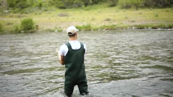 フライフィッシング中にフックを投げつける白人男性漁師のスローモーションショット ユタ州のプロボ川の真ん中に立っている — ストック動画