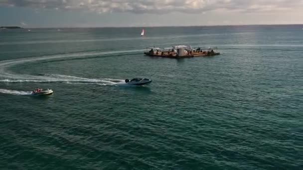パラダイス島の夕日の下で それに人々とドーナツフロートを引くスポーツボートに焦点を当てた空中ショット — ストック動画
