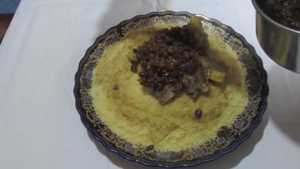 モロッコ女性は伝統的なモロッコ料理を提供しています シェフは ラドルと手を使用してクスクスの上に鍋から肉 スープ 乾燥レーズンと玉ねぎを入れています モロッコ料理 閉めろ モロッコ — ストック動画