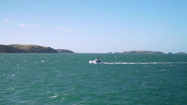 Slowmo ニュージーランドの背景に小さな島があるターコイズブルーの海に小さなボートのショットを移動する — ストック動画