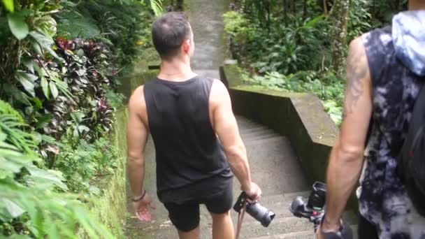 2人の若い男性がバリのジャングルの階段を歩いていて 周囲には湿り気のある緑豊かな植物があります スローモーション — ストック動画