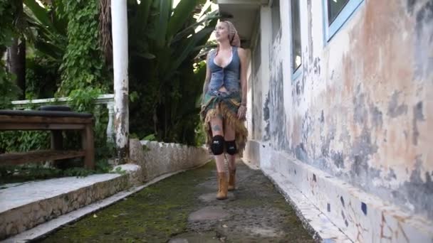 在一座废弃建筑的一条小径上 一位酷酷的 笨重的 看起来像吉普赛人的女人正朝摄像机走去 旁边是一片丛林和大自然 慢镜头 牛仔裤背心 裙子和靴子 — 图库视频影像