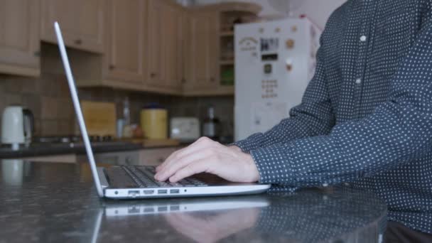 自宅で働いている間 台所のカウンターでノートパソコンに入力するスマートな服装の男 — ストック動画