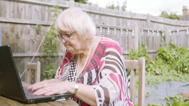 Ηλικιωμένη Γυναίκα Δακτυλογράφηση Ένα Μαύρο Φορητό Υπολογιστή Αργά Σκέψης Και — Αρχείο Βίντεο