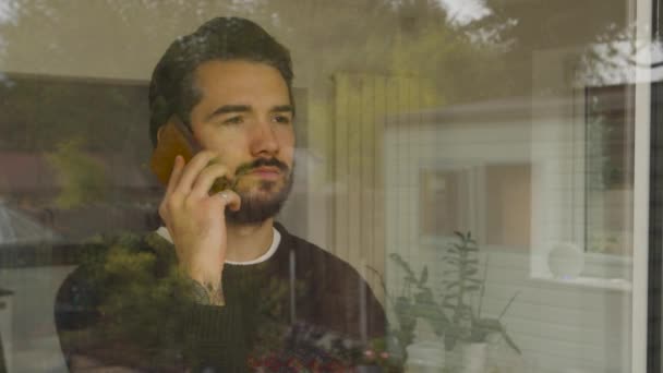 Άντρας Κοιτάζει Έξω Από Παράθυρο Μιλώντας Ένα Έξυπνο Τηλέφωνο — Αρχείο Βίντεο