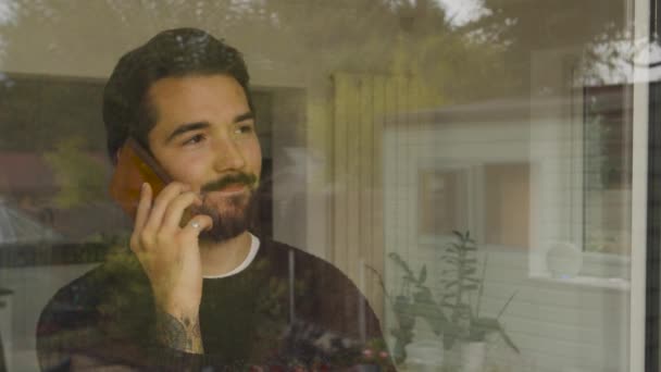 Mężczyzna Wyglądający Przez Okno Mówiący Przez Smartfon Rozłączający Się Uśmiechający — Wideo stockowe