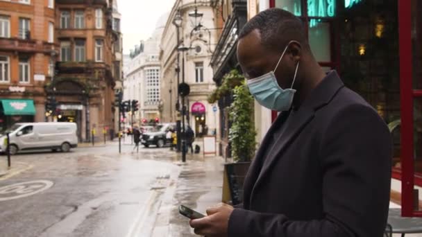 Mann Mit Medizinischer Maske Mit Smartphone Auf Belebter Straße London — Stockvideo