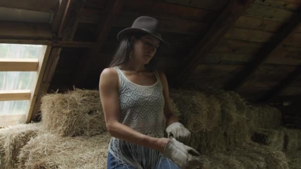 作業用手袋をはめたカウガールを追いかけ 馬に餌をやるために藁の俵を持ち上げる 室内撮影 馬小屋 — ストック動画