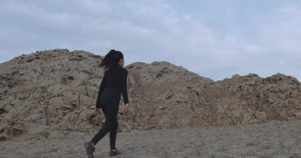 砂の山の間の砂漠を歩く黒い服を着た謎の女性の長いスローモーションショット — ストック動画