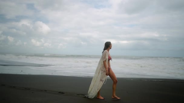 魅力的 若いです ビキニの独立した女性は バリで一人で黒砂のビーチを歩く インドネシア — ストック動画