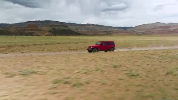 美国犹他州的红色吉普漂泊者在泥泞的路上飞驰而过半干旱沙漠 跟踪目标 — 图库视频影像