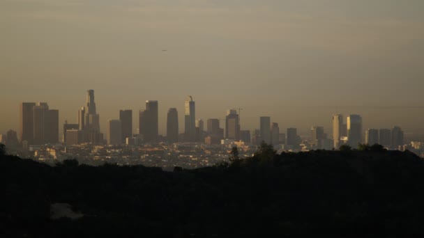 加利福尼亚州洛杉矶市中心 一个夏日的早晨 从城市西北部的山上可以看到 一架飞机飞越了标志性的城市景观 一个朦胧的灰色天空笼罩着大都市 — 图库视频影像