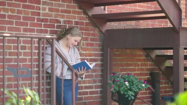 Girl Student Smiles While Reading Book Brick Wall Slow Motion — Stock Video