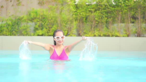 濡れた髪をした幸せなエキゾチックな女性が高級トロピカルリゾートのスイミングプールで水で遊んでいます スローモーション — ストック動画