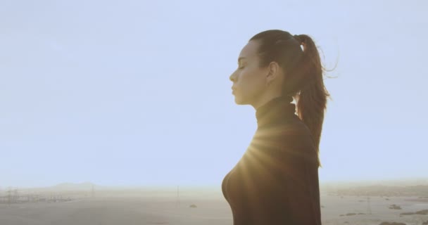 黒の服を着たプロフィールの美しい女性と縛られた髪は 太陽に対する日没で砂漠の真ん中にまっすぐ前に見えます スローモーション4K — ストック動画