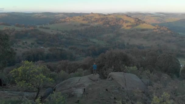 空中射击从一个站在花岗岩巨石上凝视着维多利亚时代高原地区日出美景的男人身上飞过 — 图库视频影像