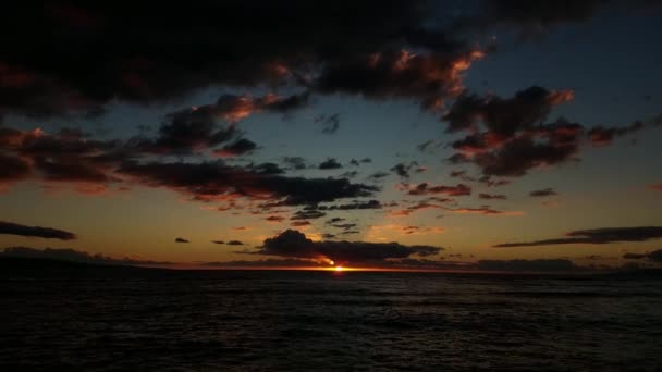 太陽が背景に沈む夕日をカメラが雲からパンし 太陽を過ぎ サーフィンから岩の多いビーチへ — ストック動画