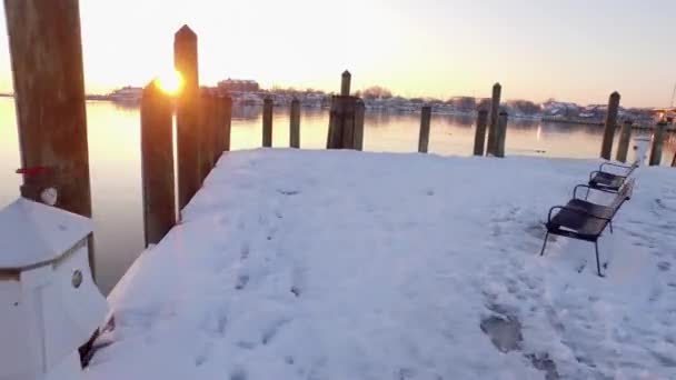 雪に覆われた桟橋は 歴史的なアナポリス メリーランド州で黄金の太陽が昇る間 杭の上や川の上で非常に低い空撮 — ストック動画