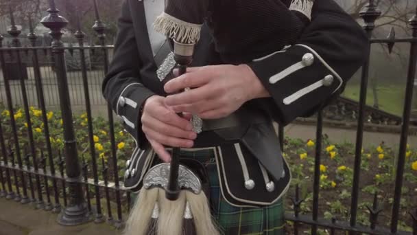 スコットランドのエディンバラにあるプリンス ストリート ガーデンのあるブラックで華やかな金属製のフェンスの隣でバグパイプを演奏しているときに 男性のスコットランドのバグパイプ手のクローズアップ — ストック動画