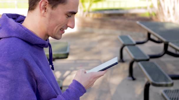 年轻的成年男性一边在公园里打电话 一边笑着浏览社交媒体 中近身 慢动作 — 图库视频影像