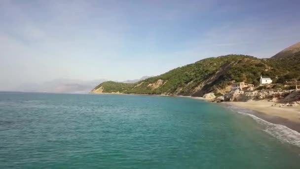 アルバニア川沿いのビーチに墜落した波から飛ぶドローンは 夏休み中に山を背景に飛んでいます — ストック動画