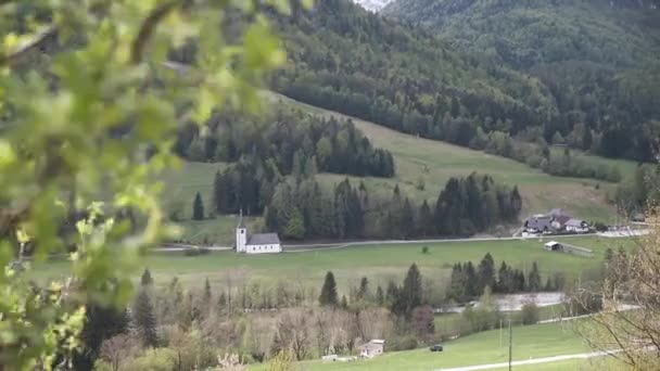 スロベニアを背景にモシュトラーナ教会とスローモーションで木が続く春のトリグラフ国立公園 — ストック動画